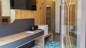 A modern bathroom with a wooden vanity, a mirror, a flat-screen TV, and a white refrigerator. - Citadel 360 Suites & Spa (Skopje)