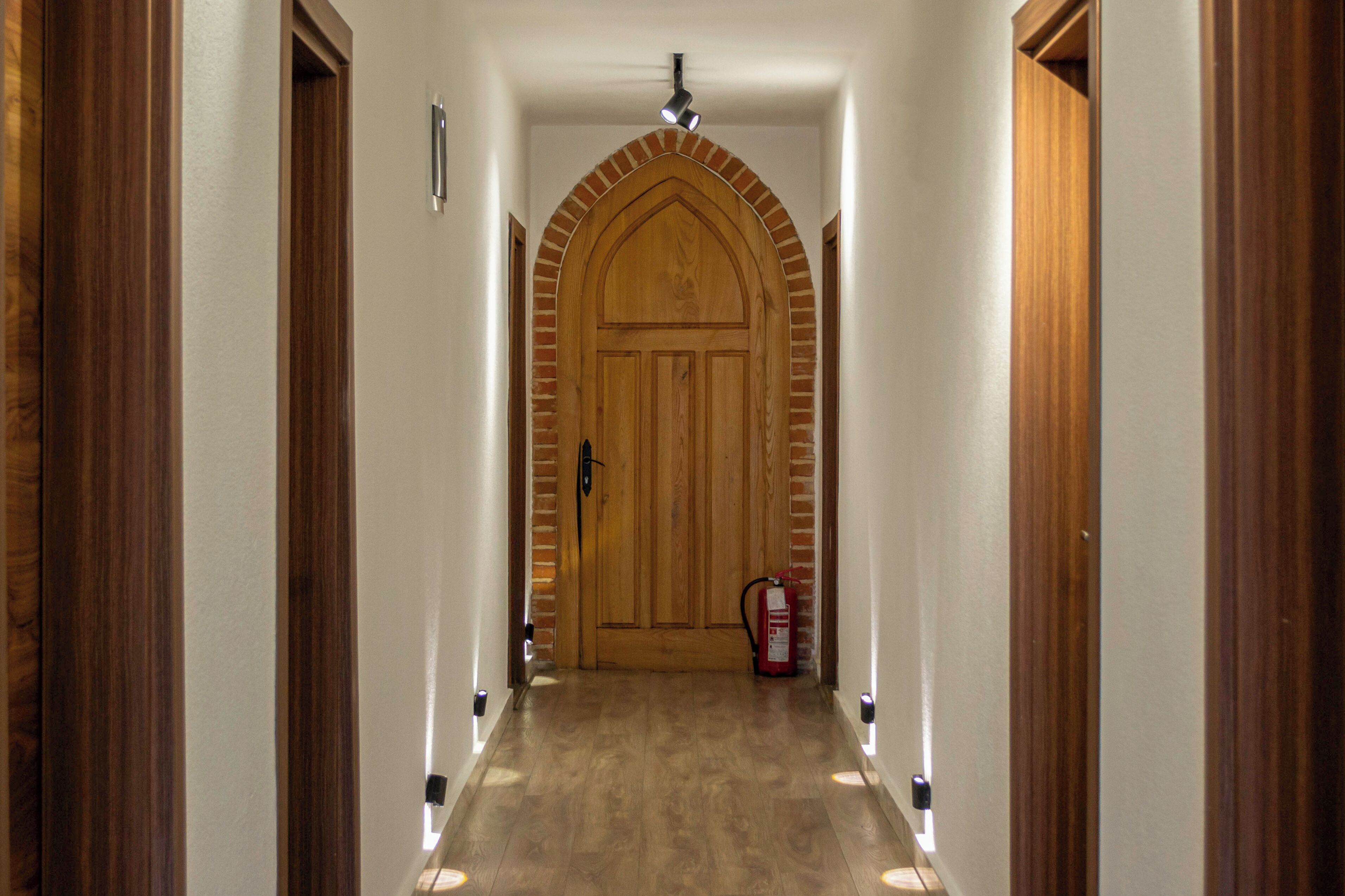 A hallway with a wooden door, a fire extinguisher, and a ceiling light fixture.