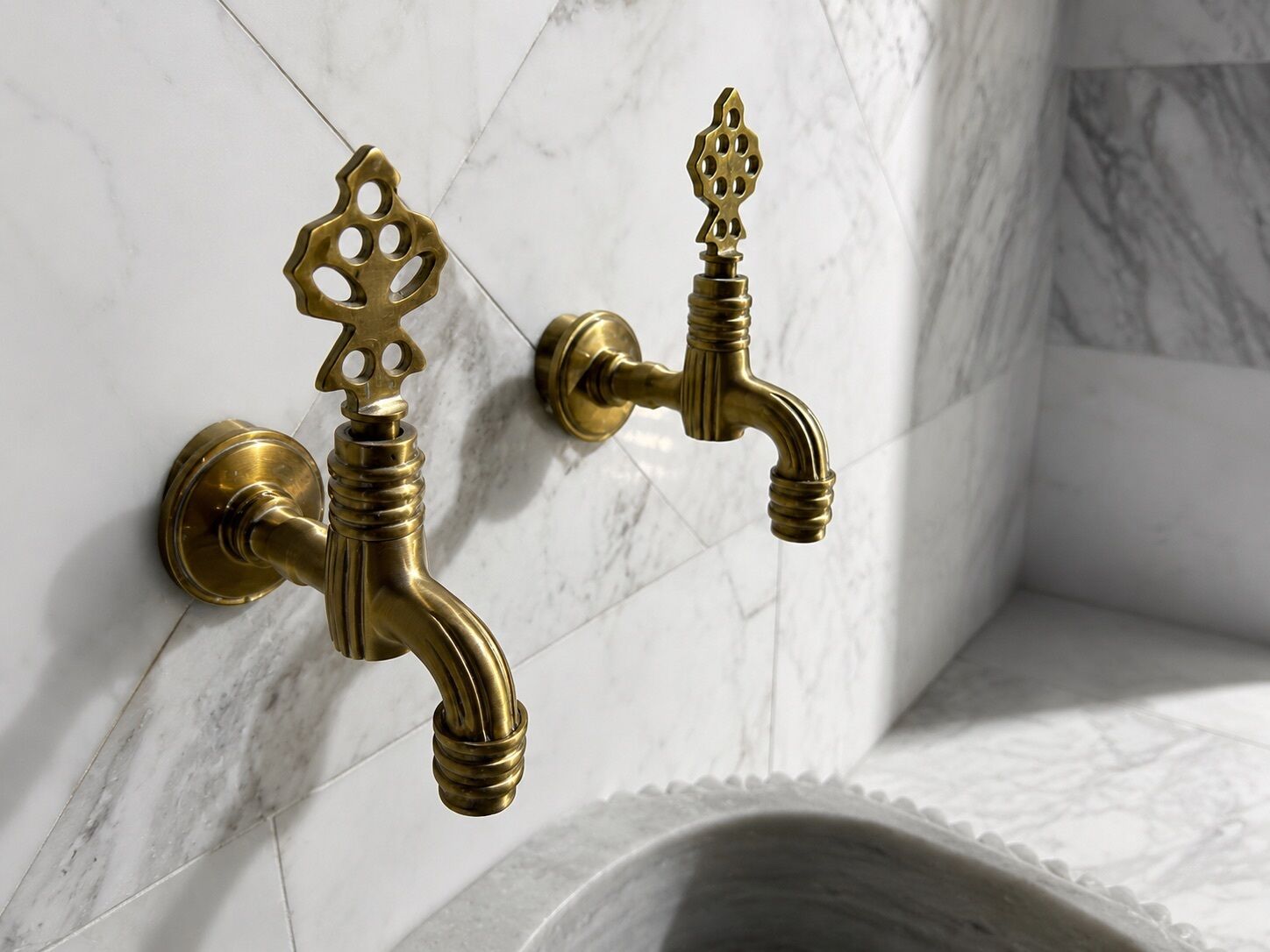 Casa de banho com duas torneiras de latão fixadas numa parede de mármore.