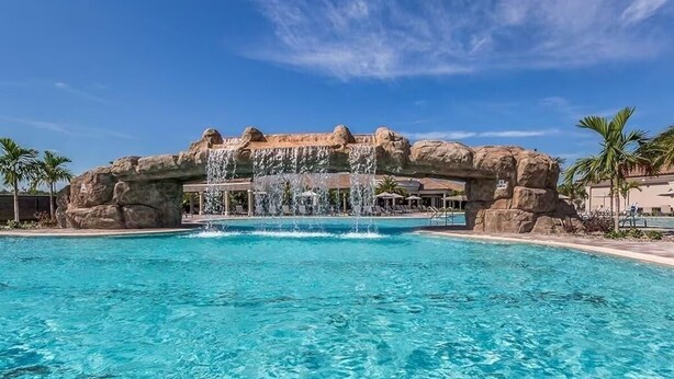 A clear pool with a waterfall feature, large rock formations, and palm trees. - Luxury 3BR Home on the 9th fairway in Lakewood National (Bradenton)