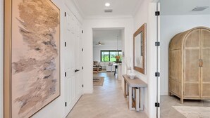 A hallway with a large abstract painting, a wooden cabinet, and a dining area in the background. - Luxury 3BR Home on the 9th fairway in Lakewood National (Bradenton)