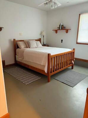 Ein Schlafzimmer mit einem Holzbett, zwei Teppichen, einem Nachttisch, einer Lampe und einem Bücherregal.