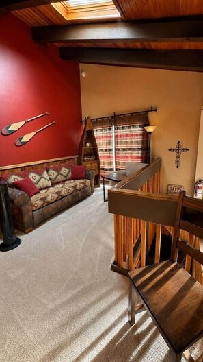A cozy living room with a red wall, a wooden bench, a sofa with patterned cushions, and a window with curtains. - Charming Stateline Condo (Round Hill Village)