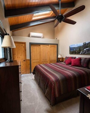 A bedroom with a bed, a ceiling fan, a window, and a painting on the wall. - Charming Stateline Condo (Round Hill Village)