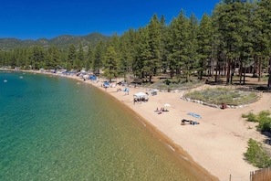 A beach with clear water, a sandy shore, and a forested area with a wooden fence. - Zephyr Cove Gem - 2-min walk to HOA Beach! (Zephyr Cove)