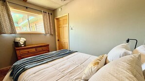 A bedroom with a bed, a dresser, a window with curtains, and a door.