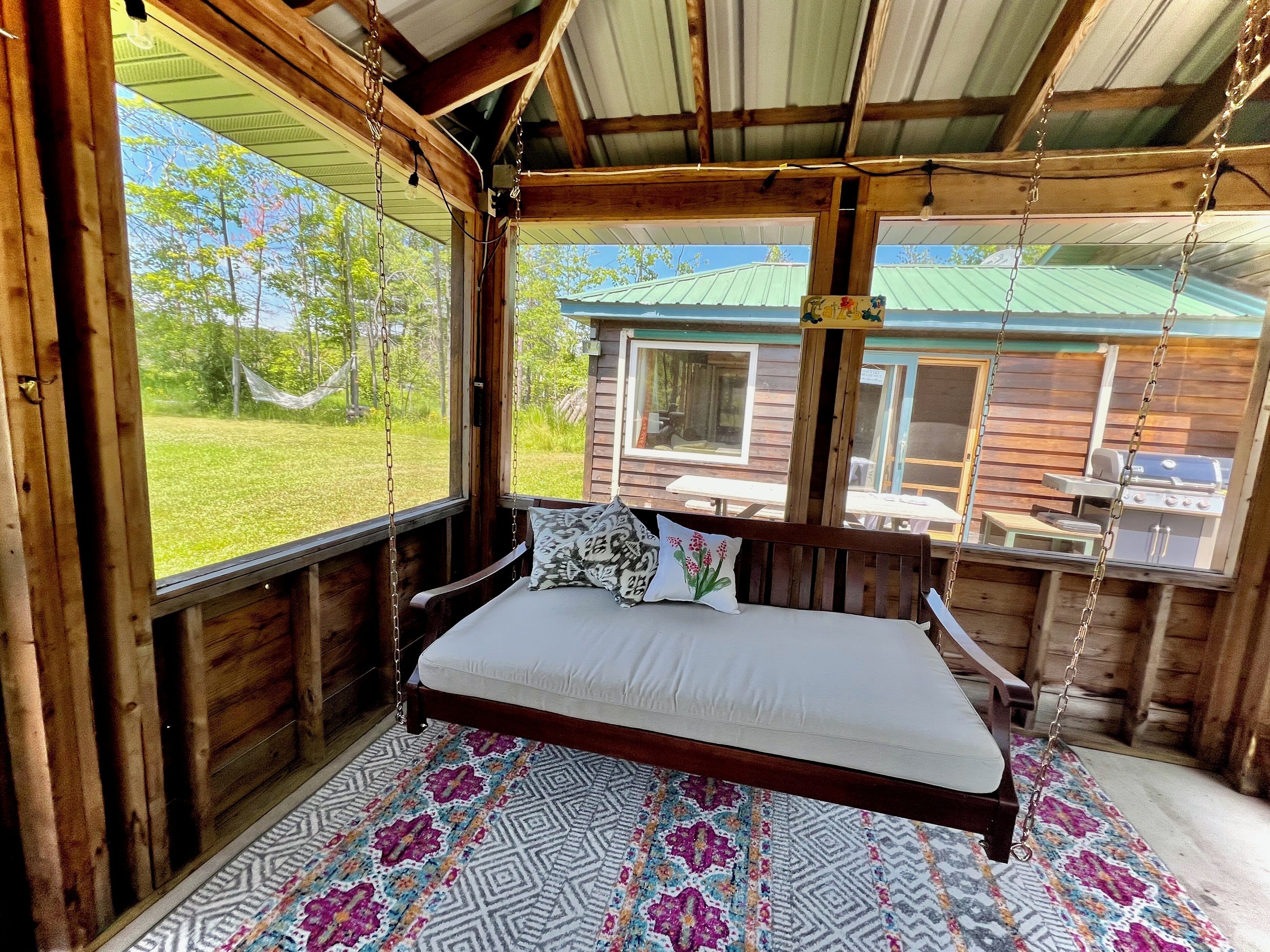 Une cabane en bois avec un lit, un hamac et une vue sur un paysage verdoyant.