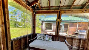 A wooden cabin with a bed, a hammock, and a view of a green landscape.