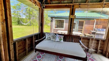 Une cabane en bois avec un lit, un hamac et une vue sur un paysage verdoyant.