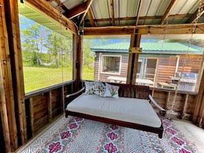 Una cabaña de madera con una cama, una hamaca y vistas a un paisaje verde.