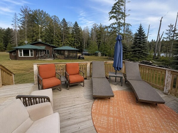 A deck with outdoor furniture, a covered picnic table, and a view of a cabin and forest.