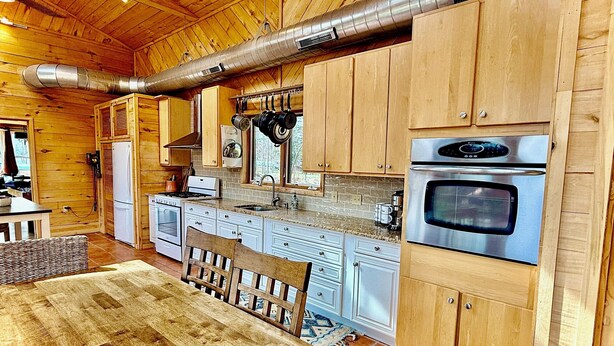 A wooden interior with a kitchen area featuring stainless steel appliances, wooden cabinets, and a large exhaust vent.