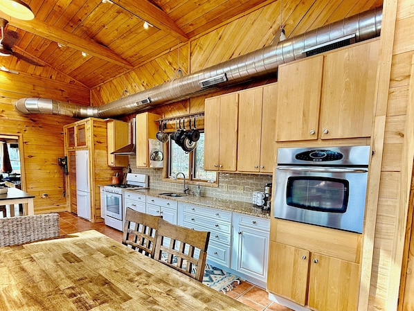 A wooden interior with a kitchen area featuring stainless steel appliances, wooden cabinets, and a large exhaust vent. - NEW!! Sandy Lakefront Cabin – Sleeps 10 with Kayaks & ATV Access (Fence)