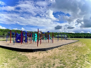 A playground with various play structures, a basketball hoop, and a fenced area. - NEW!! Sandy Lakefront Cabin – Sleeps 10 with Kayaks & ATV Access (Fence)