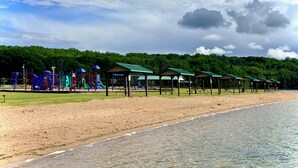 A beach with a playground, picnic tables, and covered shelters.