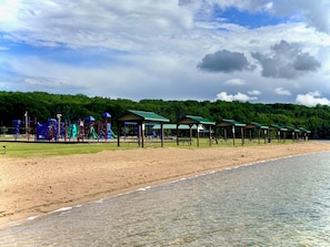 A beach with a playground, picnic tables, and covered shelters. - NEW!! Sandy Lakefront Cabin – Sleeps 10 with Kayaks & ATV Access (Fence)