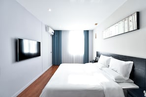A modern hotel room with a flat-screen TV, a large bed with white linens, a nightstand, and a wall-mounted artwork. - Xiamen Yisan Mamba Hotel (Xiamen)