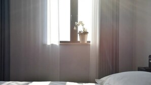 Un dormitorio con una cama, una ventana con cortinas y una planta en maceta sobre el alféizar.