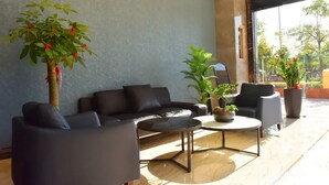 Un espacio lounge moderno con un sofá, sillones y una mesa de centro. Hay plantas en macetas y un ventanal con vistas.