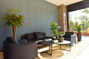 A modern lounge area with a sofa, armchairs, and a coffee table. There are potted plants and a large window providing a view. - Xiamen Yisan Mamba Hotel (Xiamen)