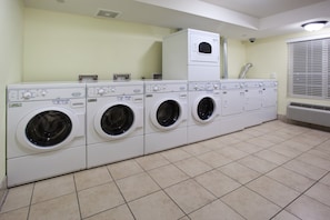 A laundry room with multiple washing machines and dryers, a vent, and a window with blinds.