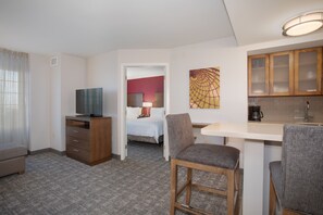 A hotel room with a bed, a TV, a desk, and a kitchenette.