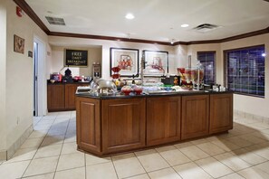 A breakfast bar with a sign offering free daily breakfast, a tiled floor, and a window with blinds.