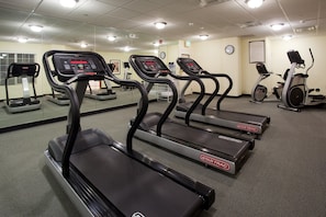 A gym with treadmills, stationary bikes, and a mirrored wall.