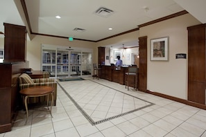 A hotel lobby with a reception desk, a waiting area with a sofa and chairs, and a tiled floor.