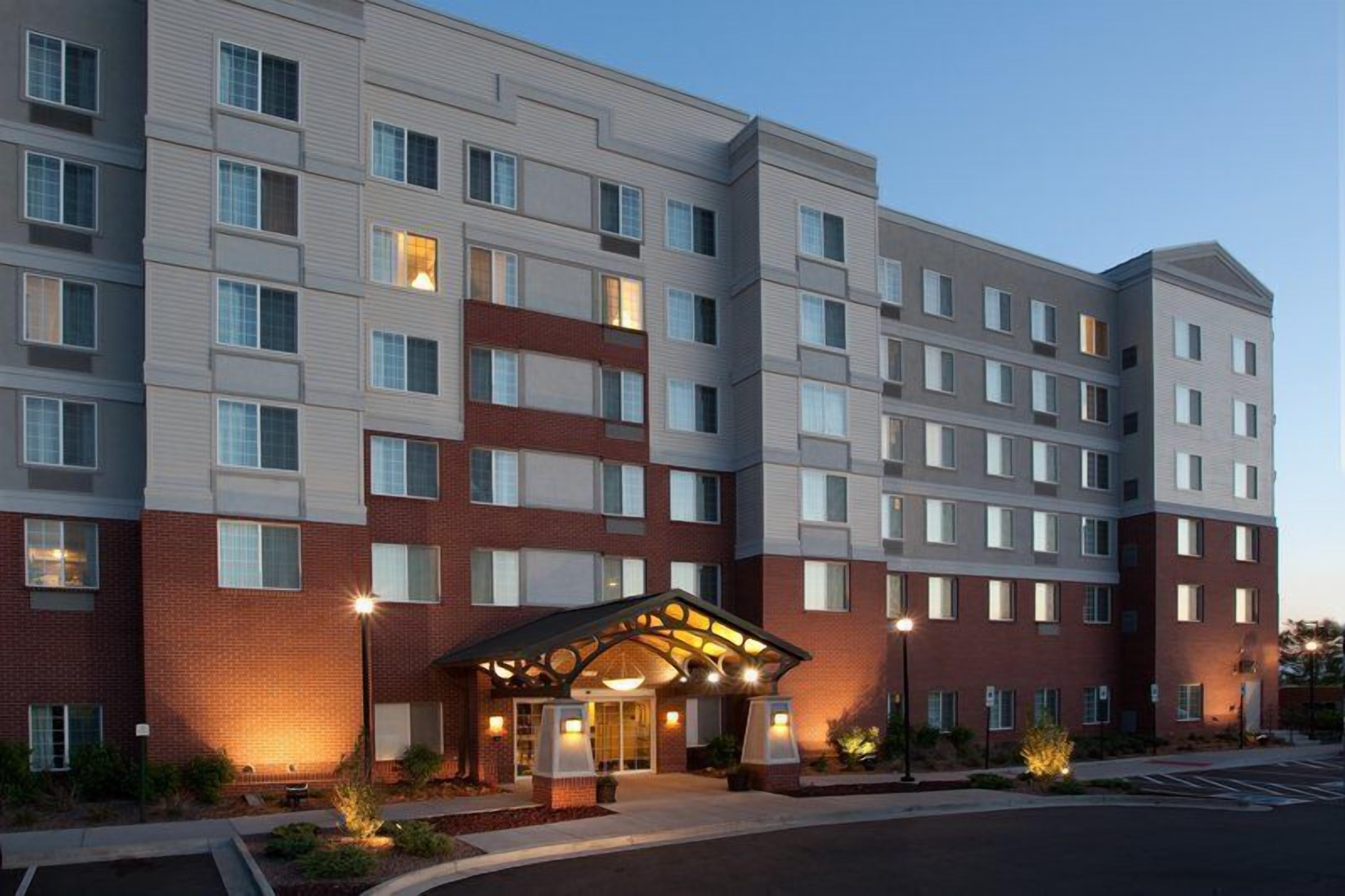 A multi-story hotel with a central entrance, a brick facade, and a parking lot.