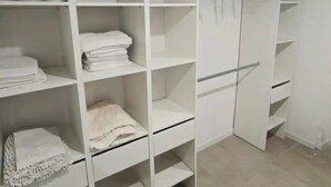 A white closet with multiple shelves and hanging space, a wooden hanger rack, and a sliding door.