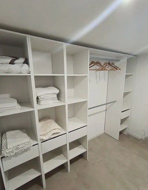 A white closet with multiple shelves and hanging space, a wooden hanger rack, and a sliding door.