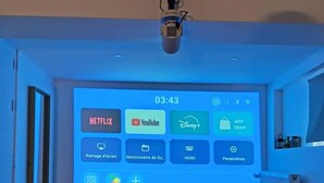 A room with a large screen displaying streaming services, a projector, and a chair.