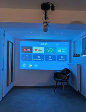 Ein Raum mit einem großen Bildschirm, der Streaming-Dienste anzeigt, einem Projektor und einem Sessel.