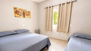 Una habitación con dos camas, una ventana con cortinas, un cuadro colgado en la pared y un pequeño estante.