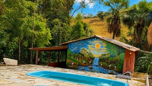 Una piscina con un mural, rodeada de árboles y un patio de piedra.