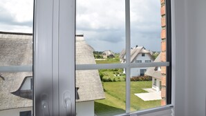 A window with a view of a residential area, including houses with thatched roofs and a brick wall. - Sturmvogel Vacation Home (Dranske)