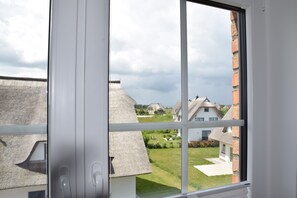 Ein Fenster mit Blick auf eine Wohngegend, darunter Häuser mit Strohdächern und eine Backsteinmauer.