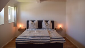 A bedroom with a bed, two bedside tables, a window, and a ceiling with exposed beams. - Sturmvogel Vacation Home (Dranske)