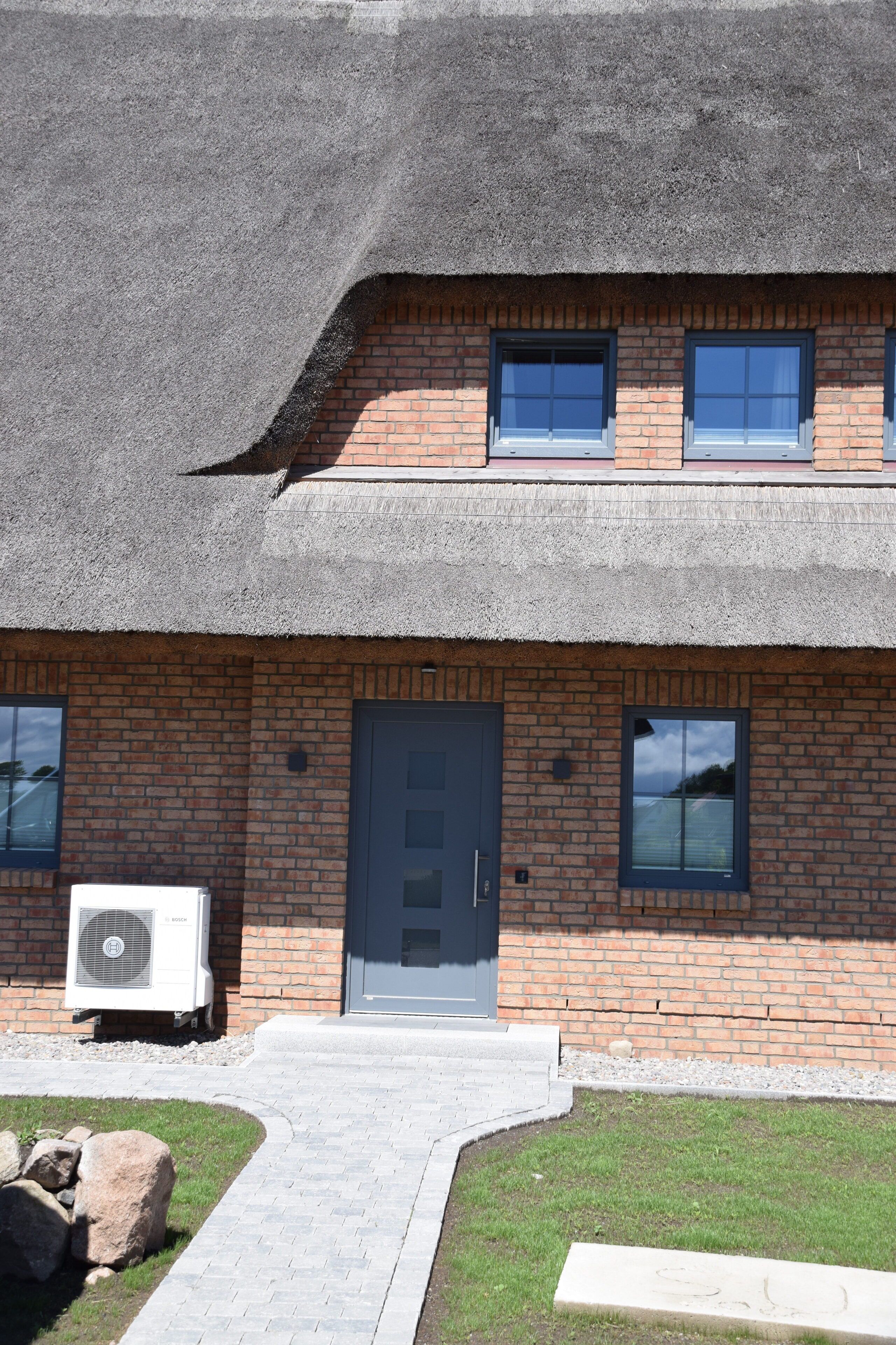 Een gebouw met twee verdiepingen, een bakstenen gevel, een grijze deur en een klein raam op de bovenverdieping.