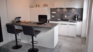 A modern kitchen with a central island, two bar stools, a coffee machine, and a built-in oven. - Sturmvogel Vacation Home (Dranske)