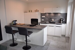 Eine moderne Küche mit einer zentralen Kochinsel, zwei Barhocker, einer Kaffeemaschine und einem eingebauten Backofen.