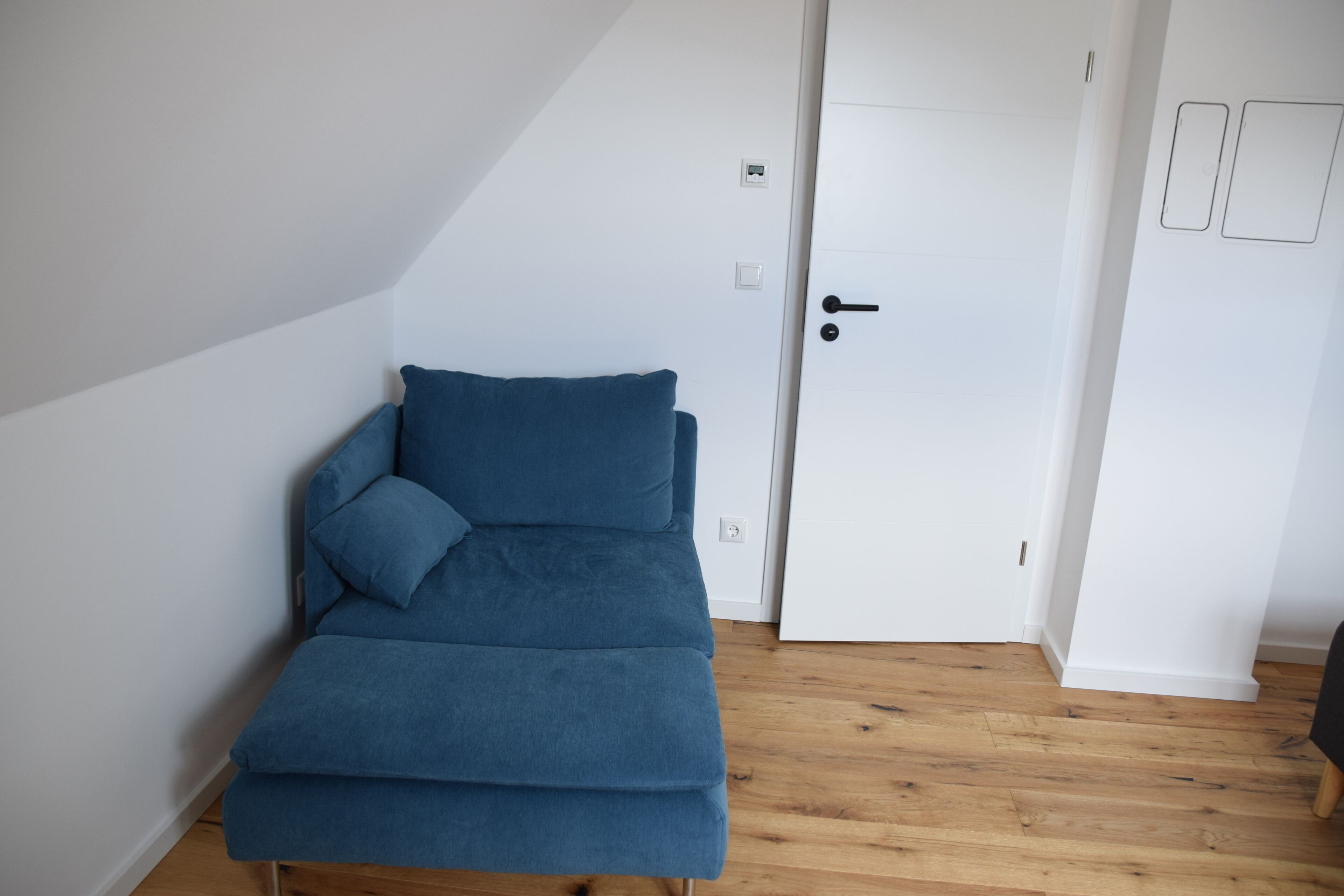 Une pièce avec un canapé bleu, une porte blanche et un plancher en bois.