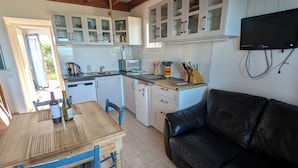 A kitchen with wooden beams, white cabinets, a dining table with chairs, a black leather couch, and a television mounted on the wall. - CHEZ NICO: A breathtaking view of the Atlantic Ocean. The dune is your garden. (Soulac-sur-Mer)