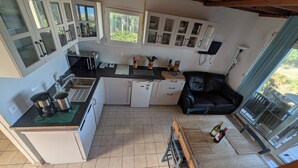 A compact kitchen with a dining area, a refrigerator, a coffee maker, and a dining table with bottles. - CHEZ NICO: A breathtaking view of the Atlantic Ocean. The dune is your garden. (Soulac-sur-Mer)