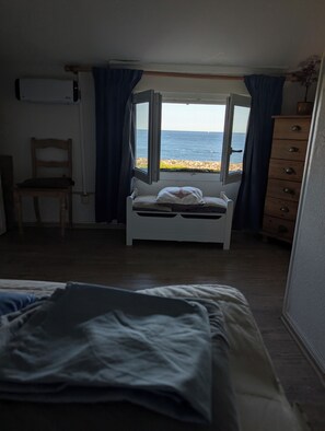 Ein Schlafzimmer mit Bett, Stuhl, Schminktisch und einem Fenster mit Meerblick.