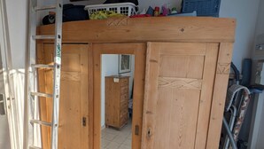 Une pièce avec une armoire en bois, une échelle, un aspirateur et un sol carrelé.