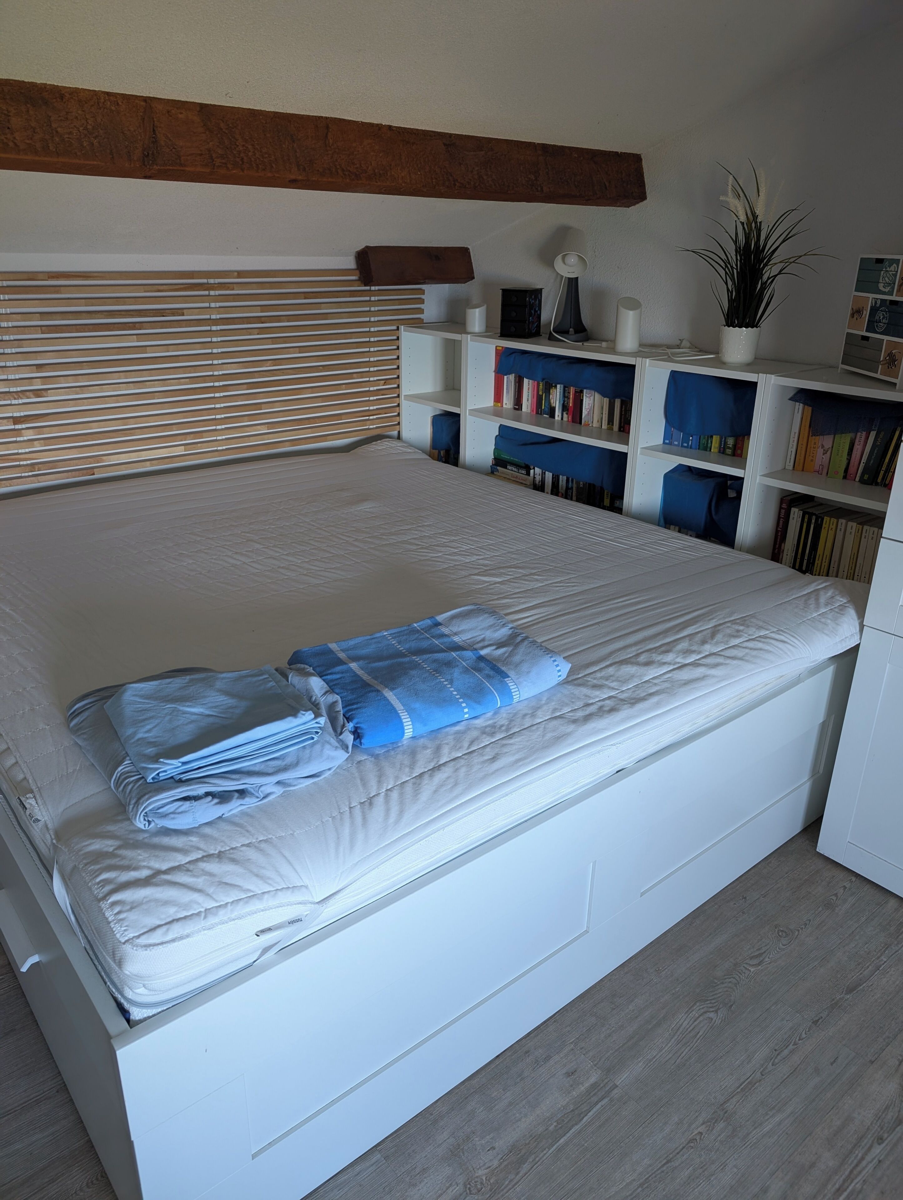 A neatly made bed with a blue blanket, a wooden headboard, and a white wardrobe.