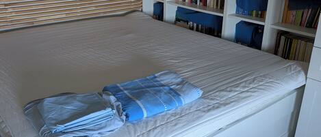 A neatly made bed with a blue blanket, a wooden headboard, and a white wardrobe.