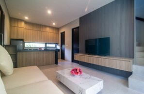 Een moderne woonkamer met een bank, een marmeren salontafel, een televisie, en een keuken met houten kastjes en een inbouwoven.